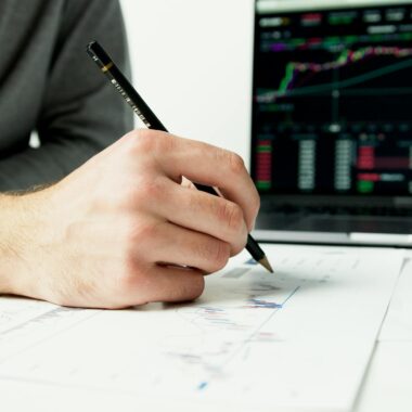 Close-up of a person analyzing financial charts with a laptop displaying stock market data.