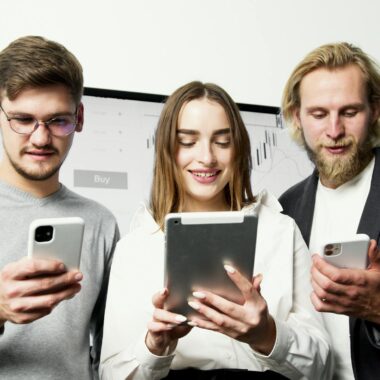 Three professionals using digital devices for financial analysis in an office setting.
